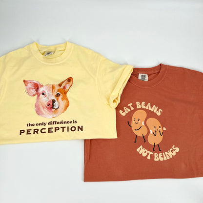 Terracotta colored vegan activism shirt featuring "Eat Beans Not Beings" graphic next to a yellow vegan activism shirt