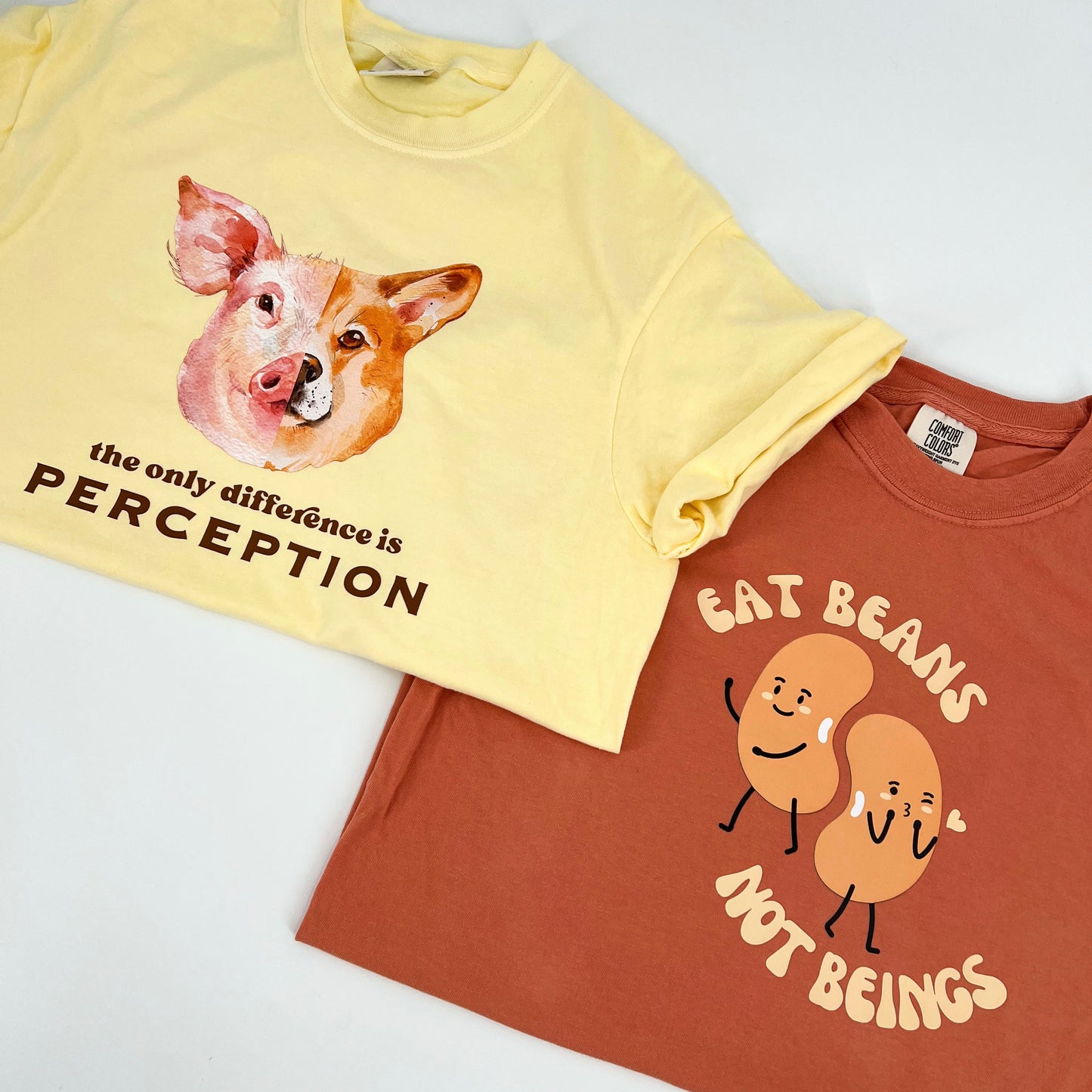 Terracotta colored vegan activism shirt featuring "Eat Beans Not Beings" graphic next to a yellow vegan activism shirt